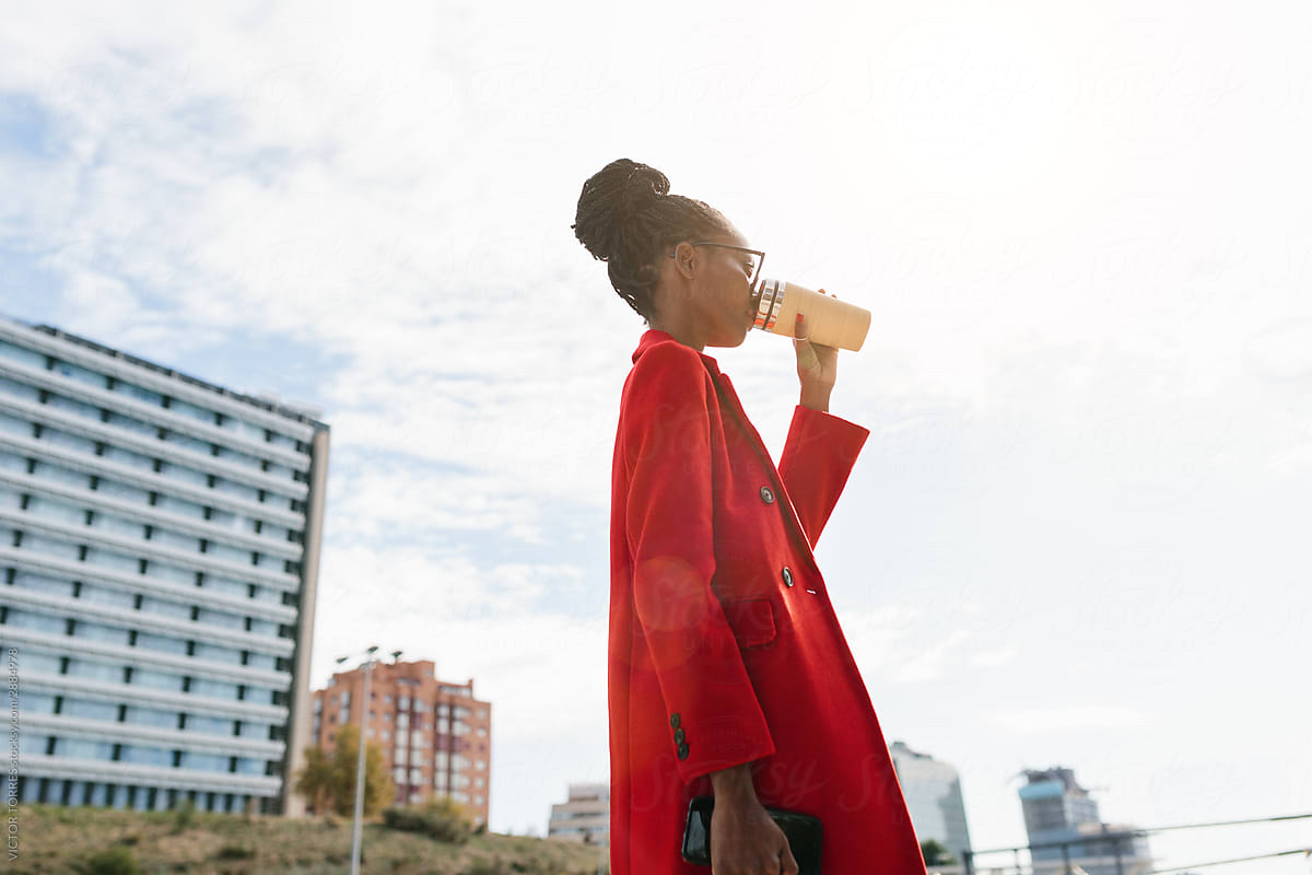 Thirsty black woman in sunglasses and coat drinking from bottle