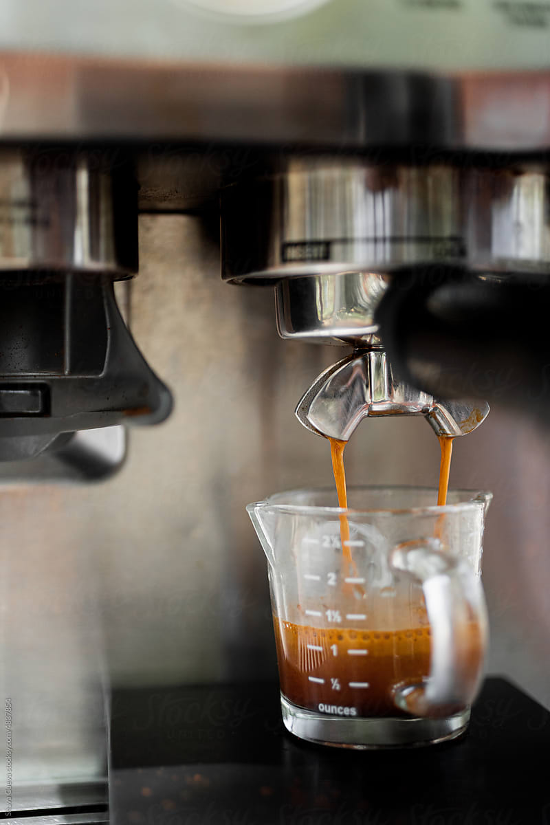 Coffee maker pouring  espresso into glass mug