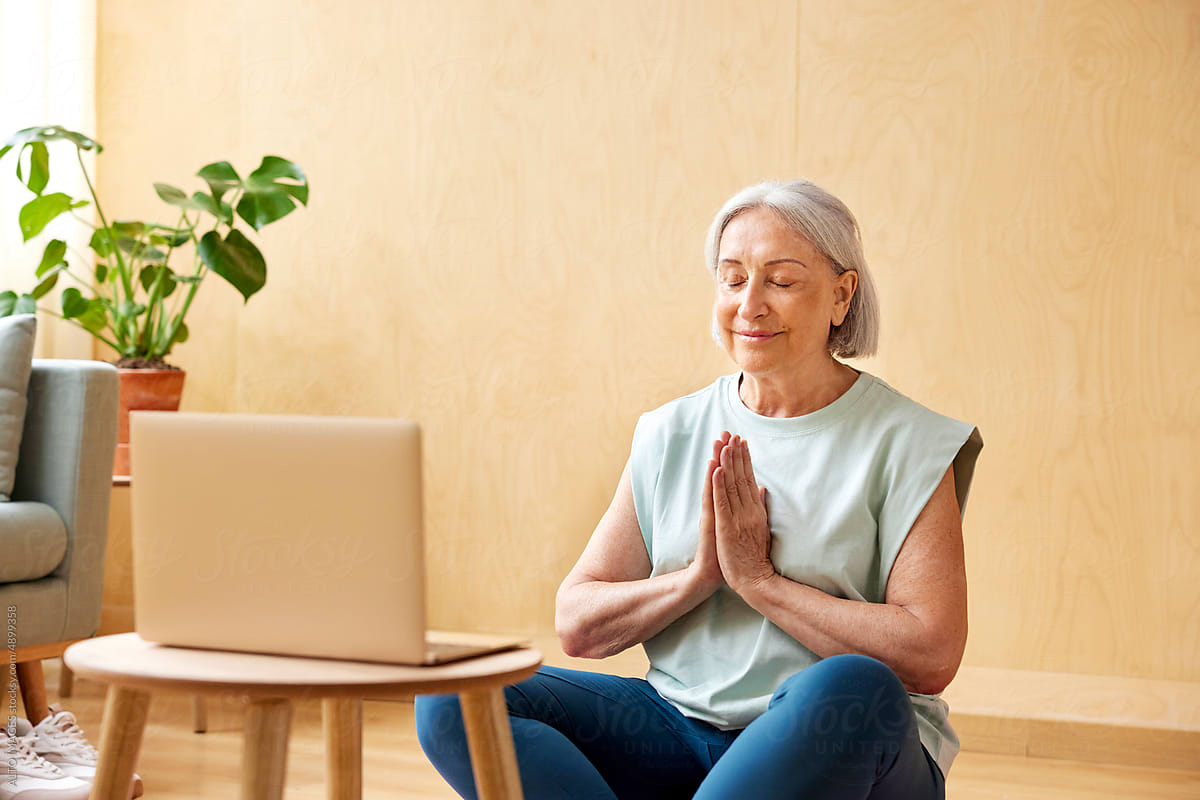 Mature woman meditating near laptop