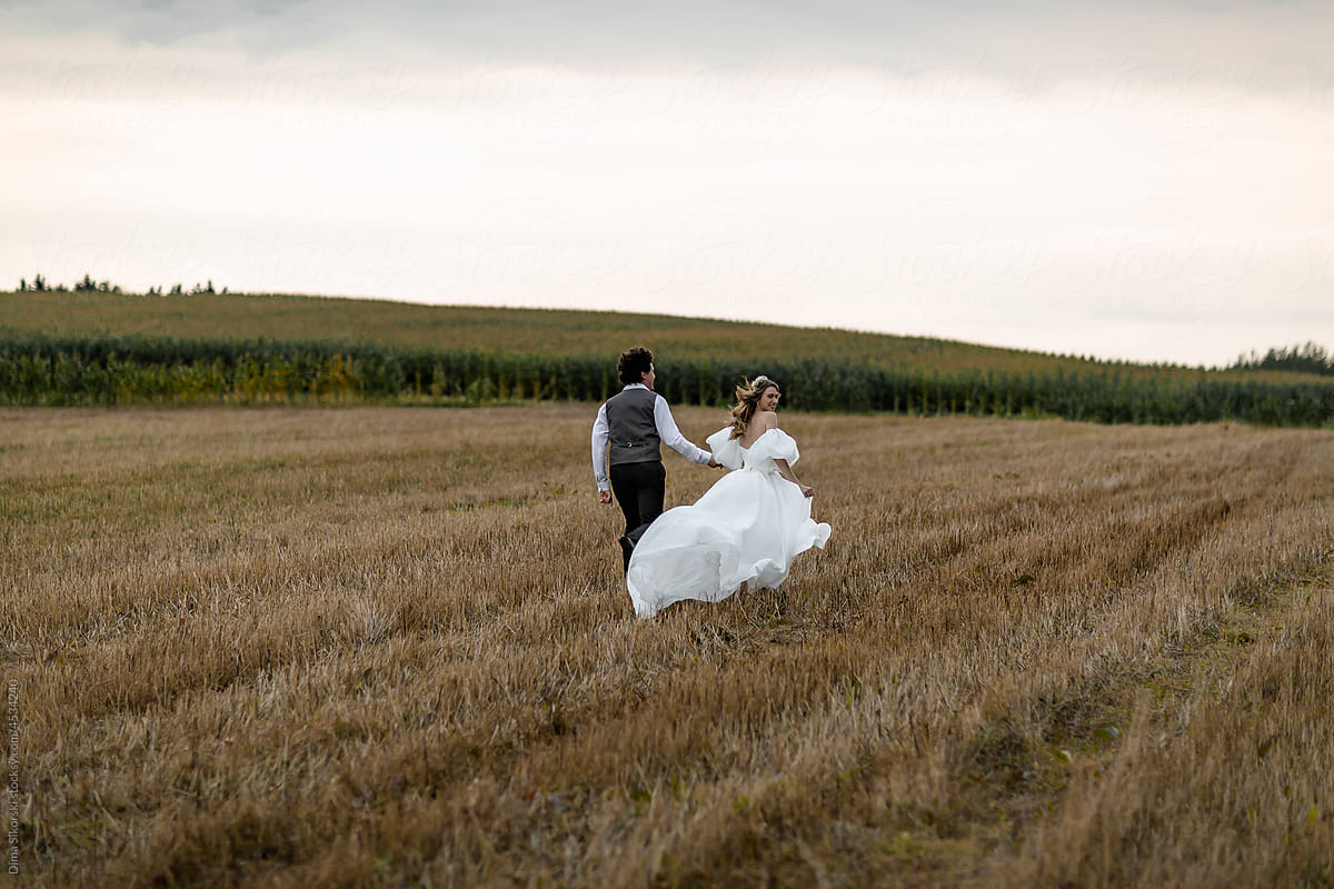 The bride and groom run through a picturesque field on the wedding day