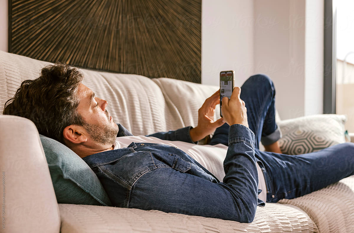 Man with smartphone resting on sofa