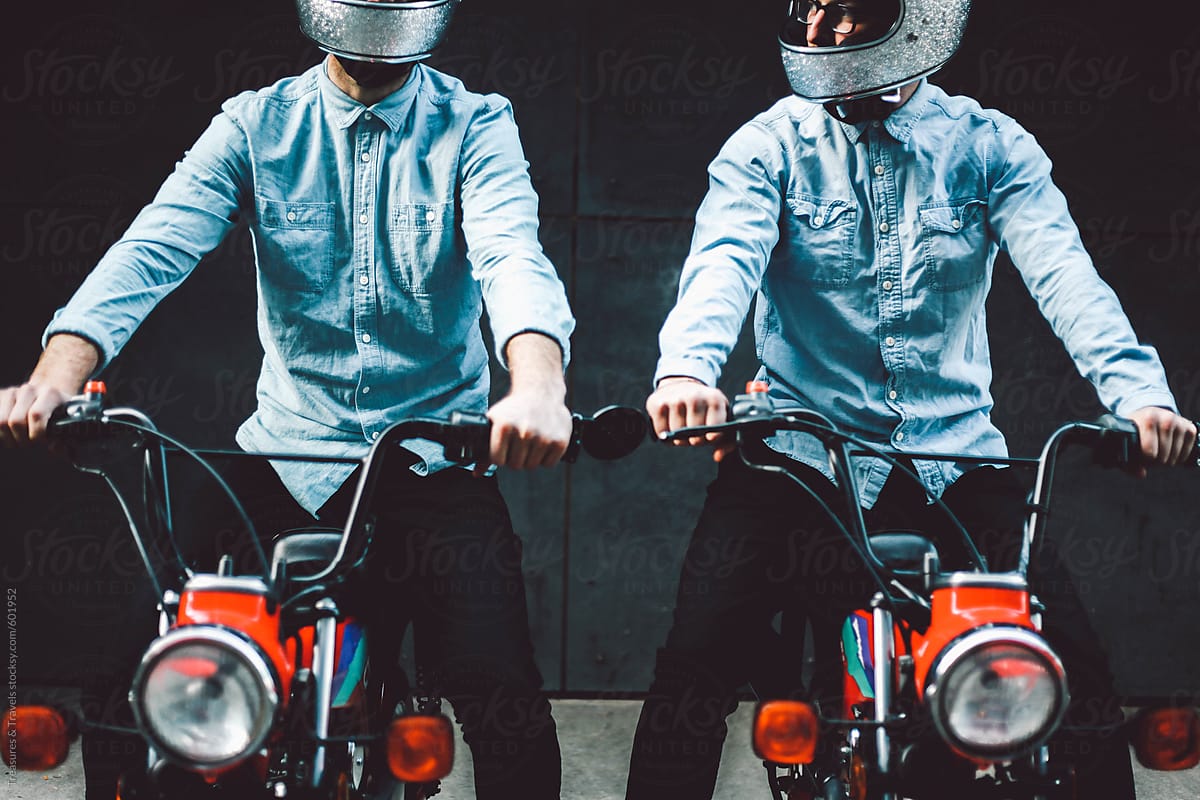 Two young men sitting on motorcycles in alleyway