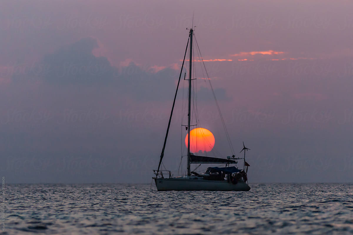 huge setting sun over a small sailboat