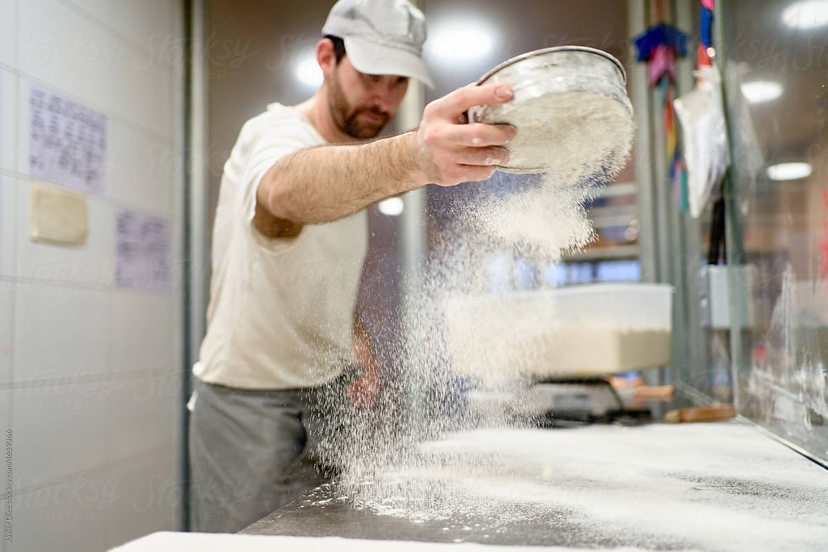 Male baker scattering flour on table