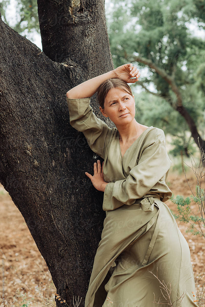 Woman in comfortable dress leaning on an oak tree