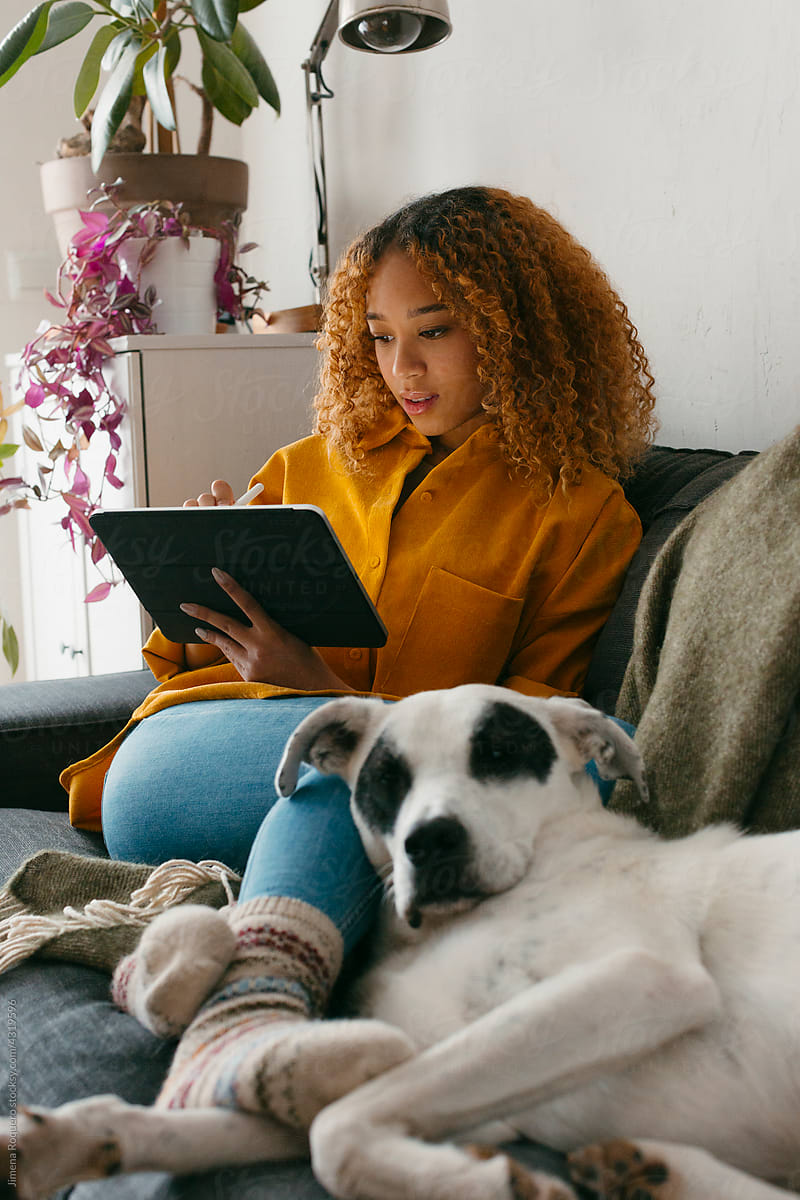 Teenager at home living room using tablet with dog
