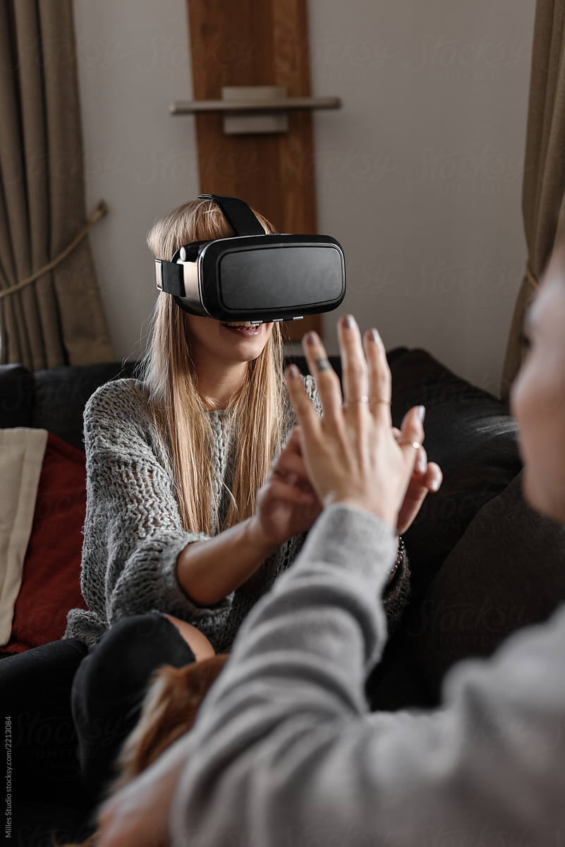 Woman in VR glasses touching hand of friend