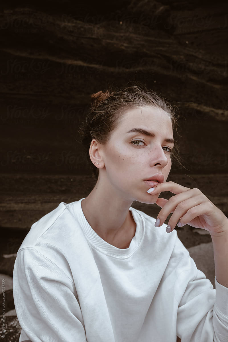 portrait of a girl in a white sweater sitting in a pensive pose on the beach