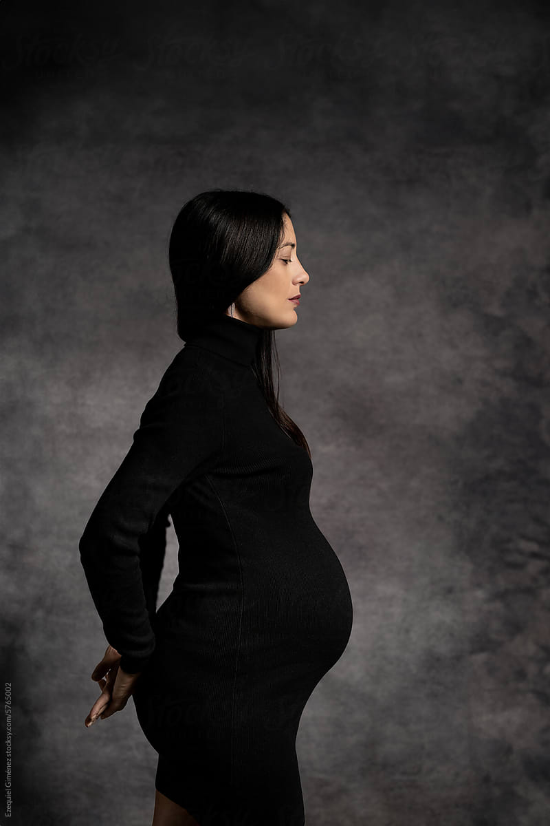 Graceful pregnant woman standing with hands behind back