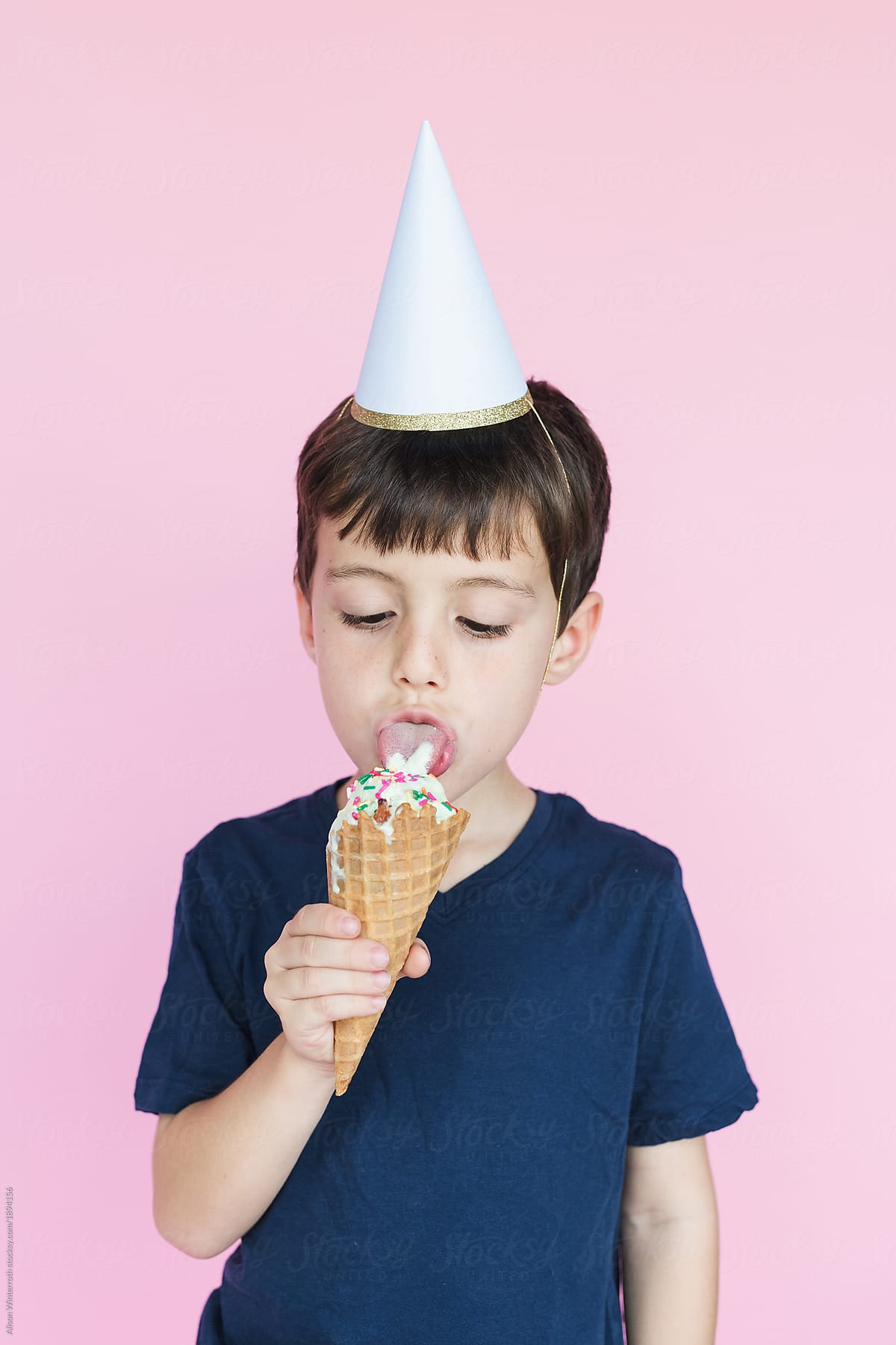 A Boy Digs In To An Ice Cream Cone With A Birthday Hat On His Head