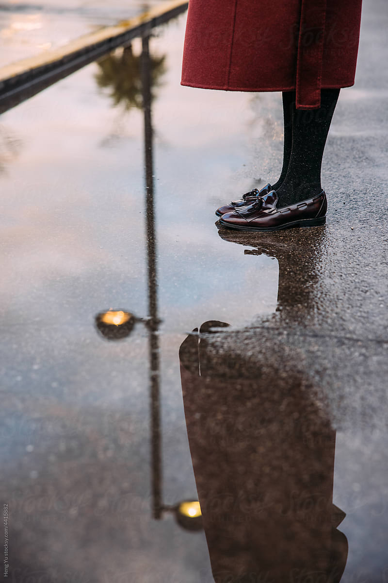 a woman standing by the puddle with lamp reflection.