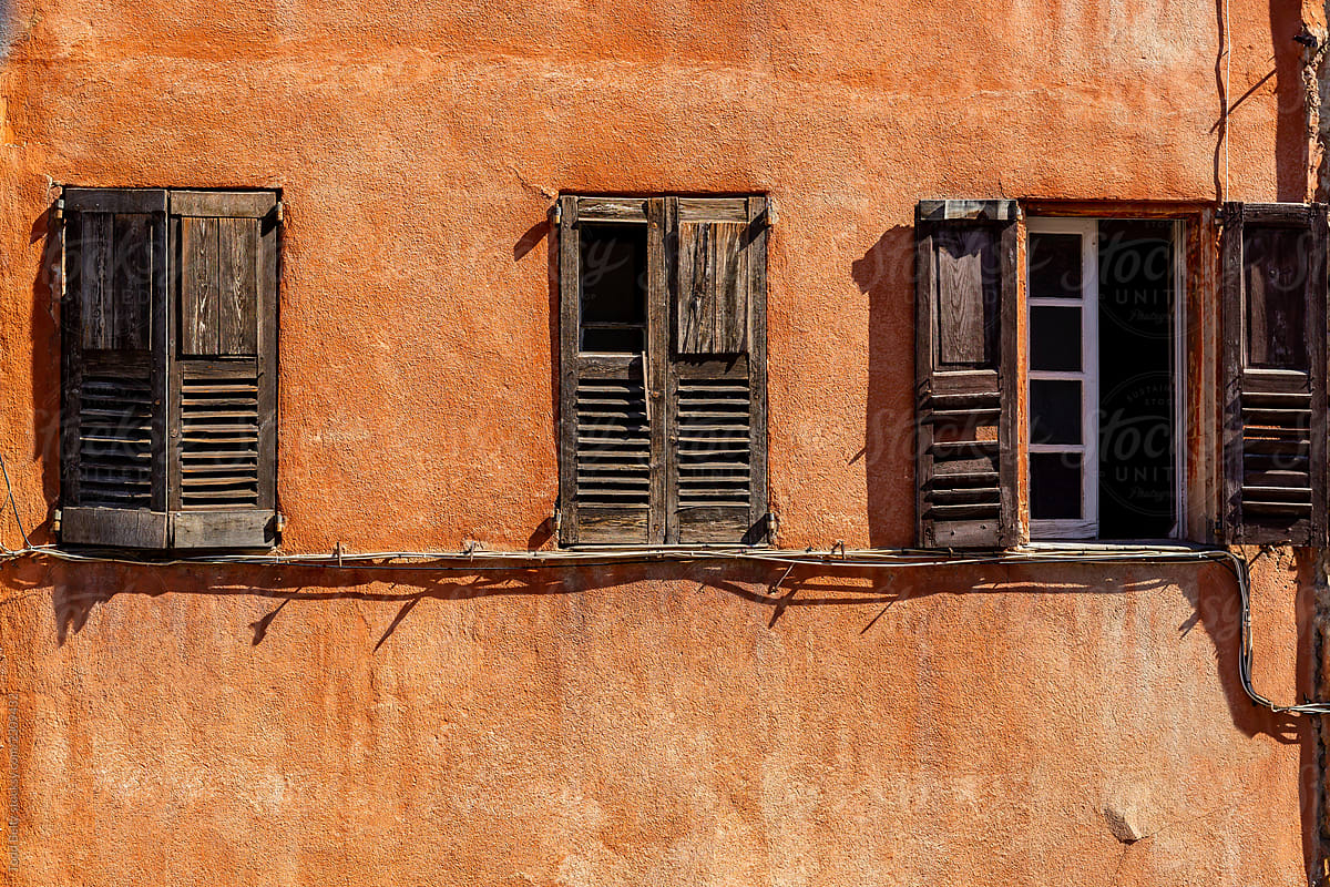 Old wooden windows on a faded orange coloured wall.