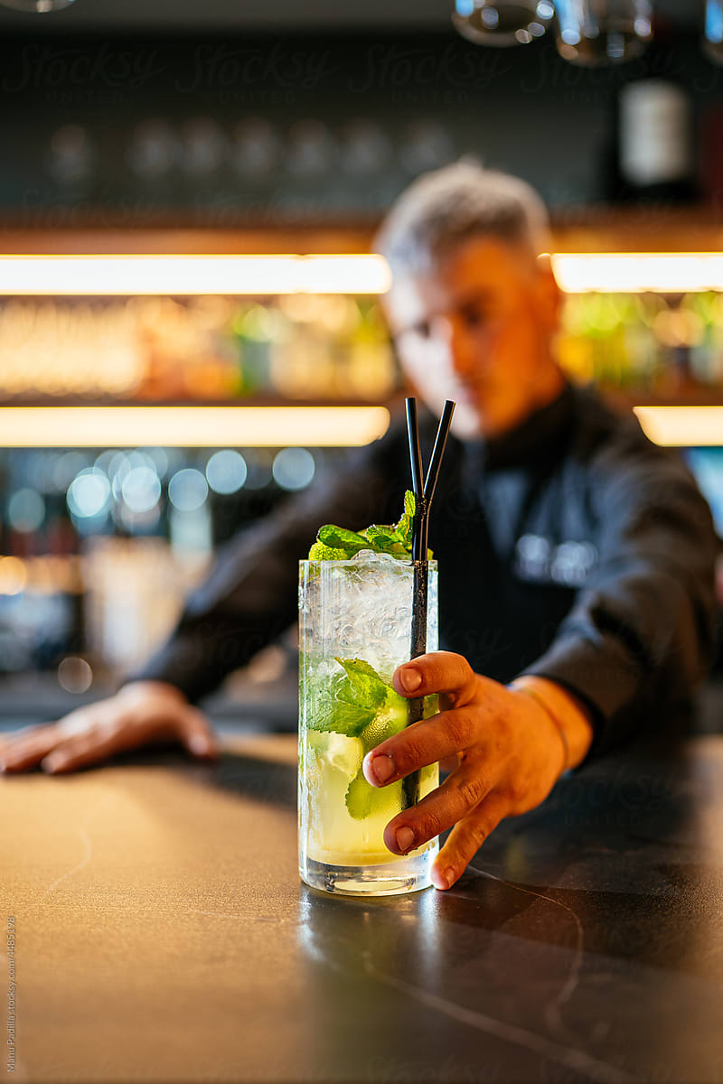 Bartender serving cold glass of mojito at counter