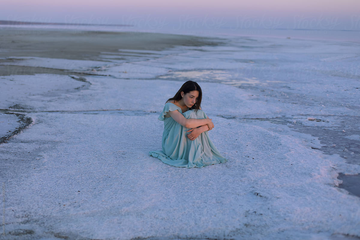 girl in a turquoise dress sitting in the snow at sunset
