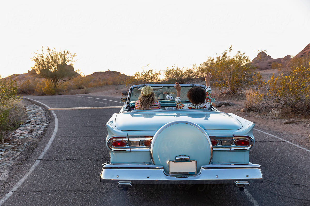 Two Beautiful Girls on Desert Road trip driving down road in classic car