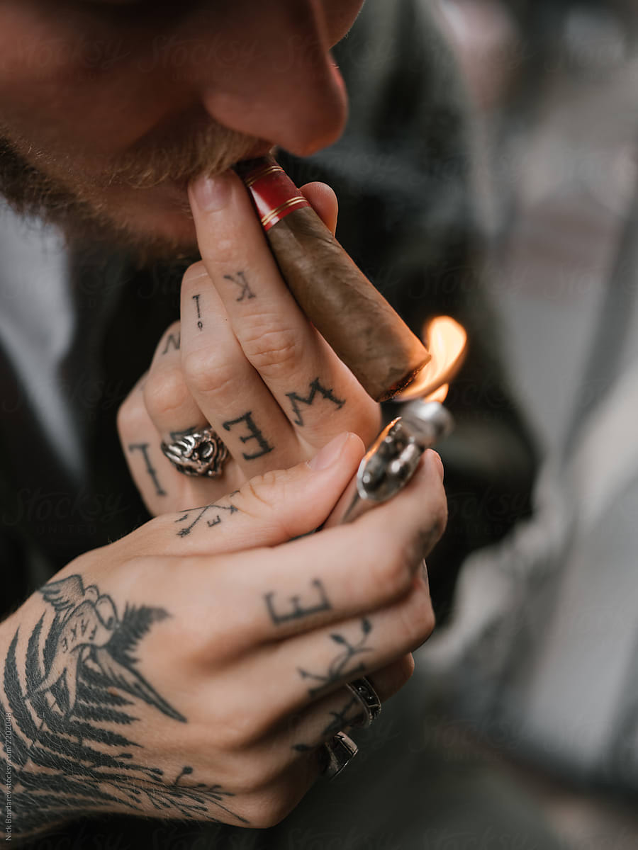 Handsome tattooed man lighting cigar