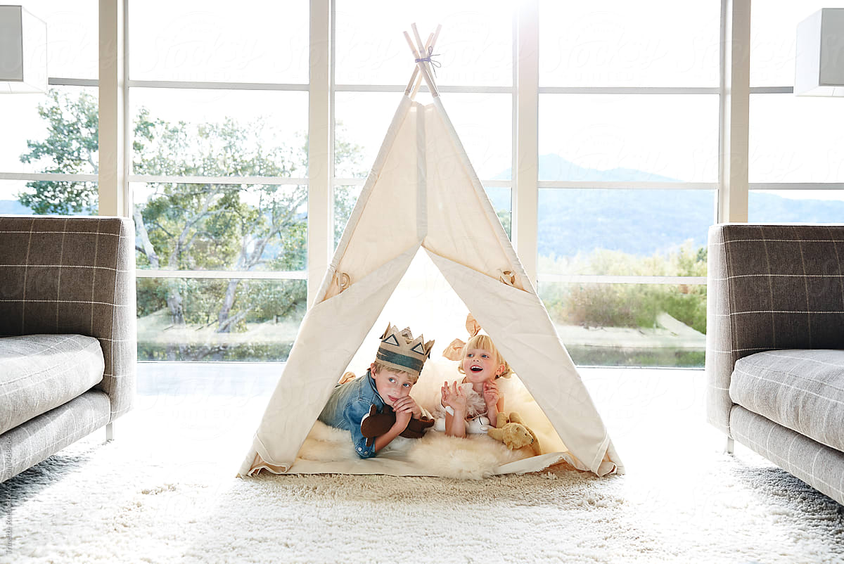 Siblings playing in teepee tent in living room