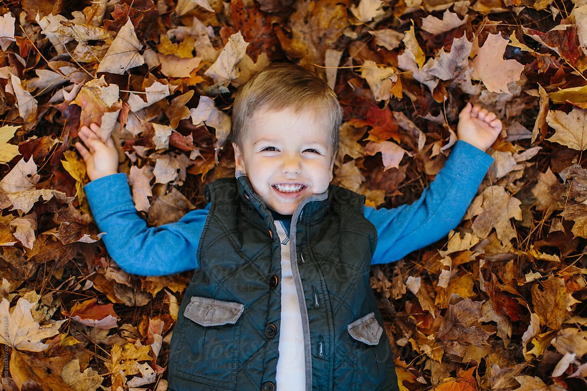 Cute young boy laying on the ground covered in leaves