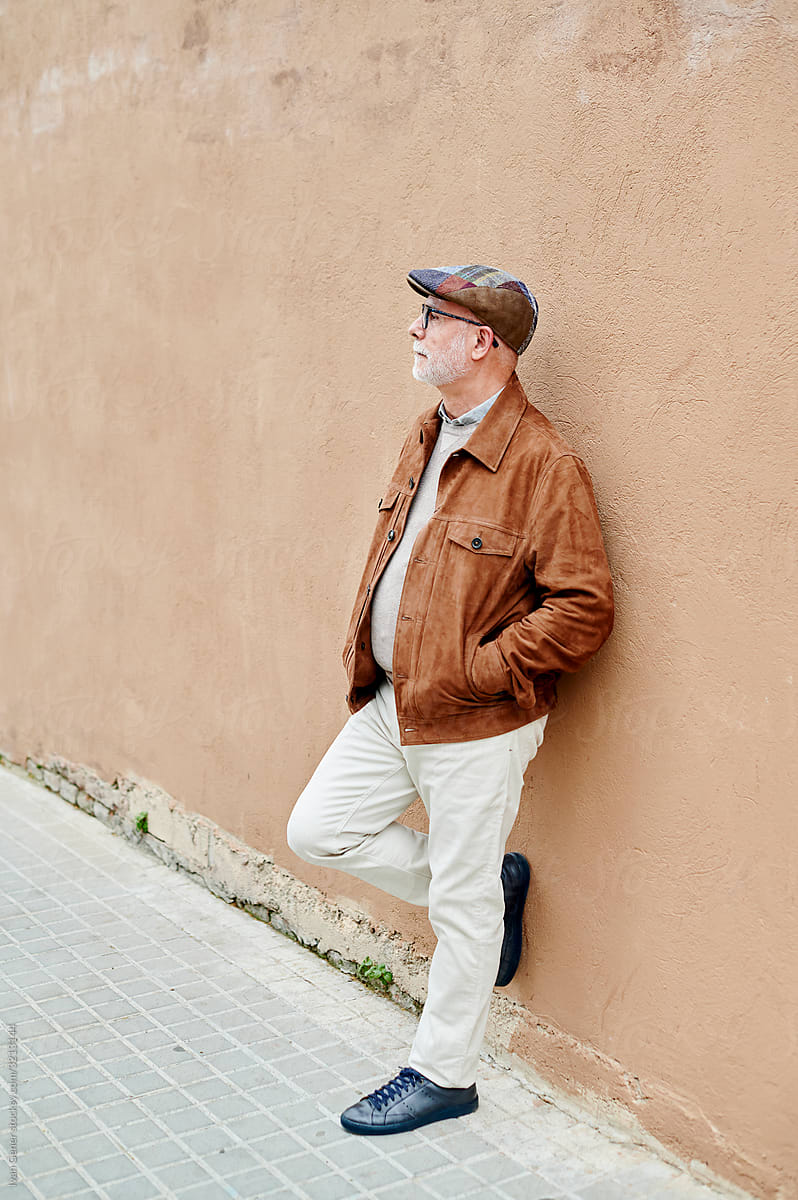 Senior man leaning against a wall outside