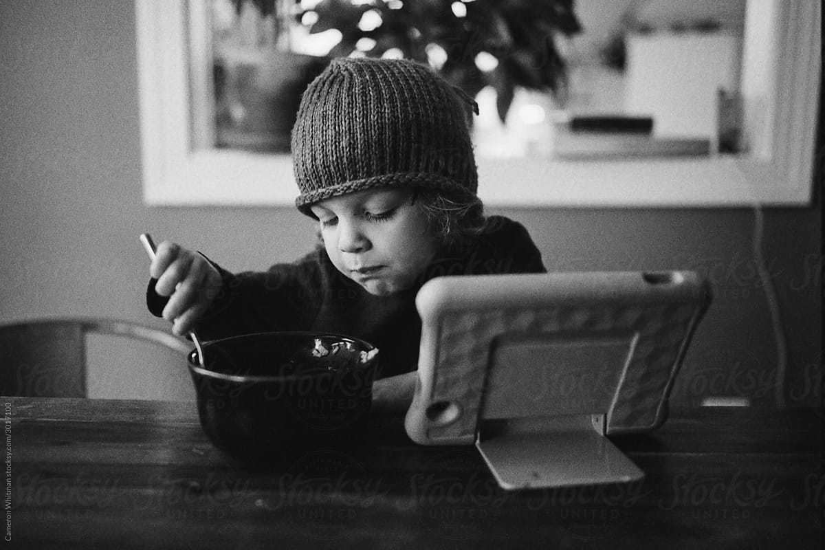 Boy eats his oatmeal while watching cartoons on his tablet