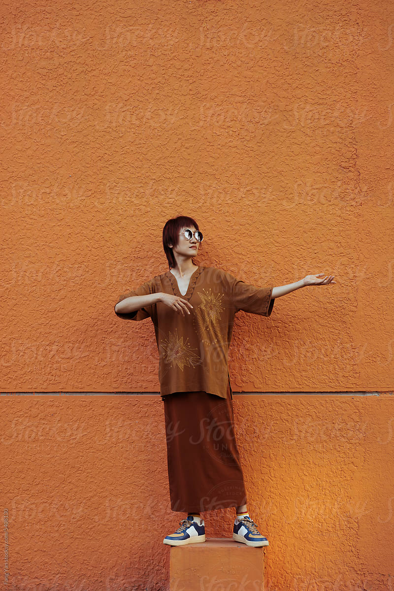 Woman Envisions Violin in playful pose by Orange Wall