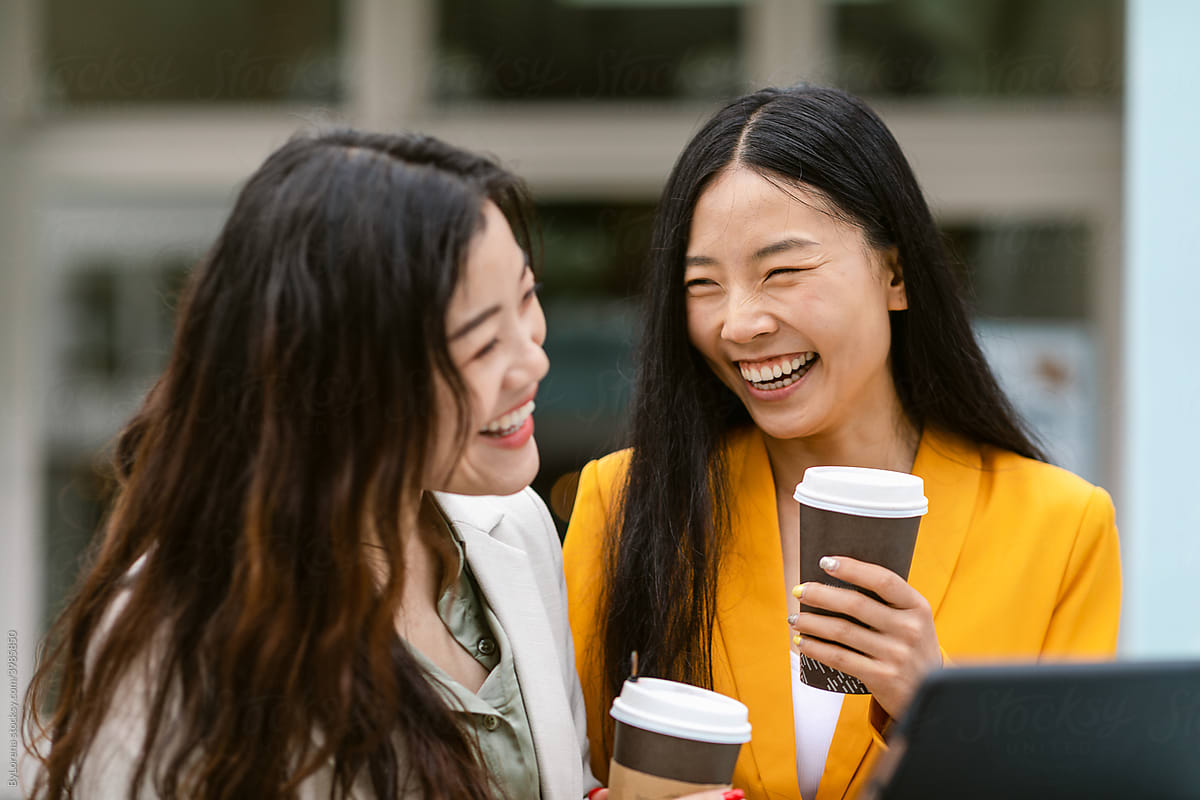 Happy Chinese women with coffee laughing on street