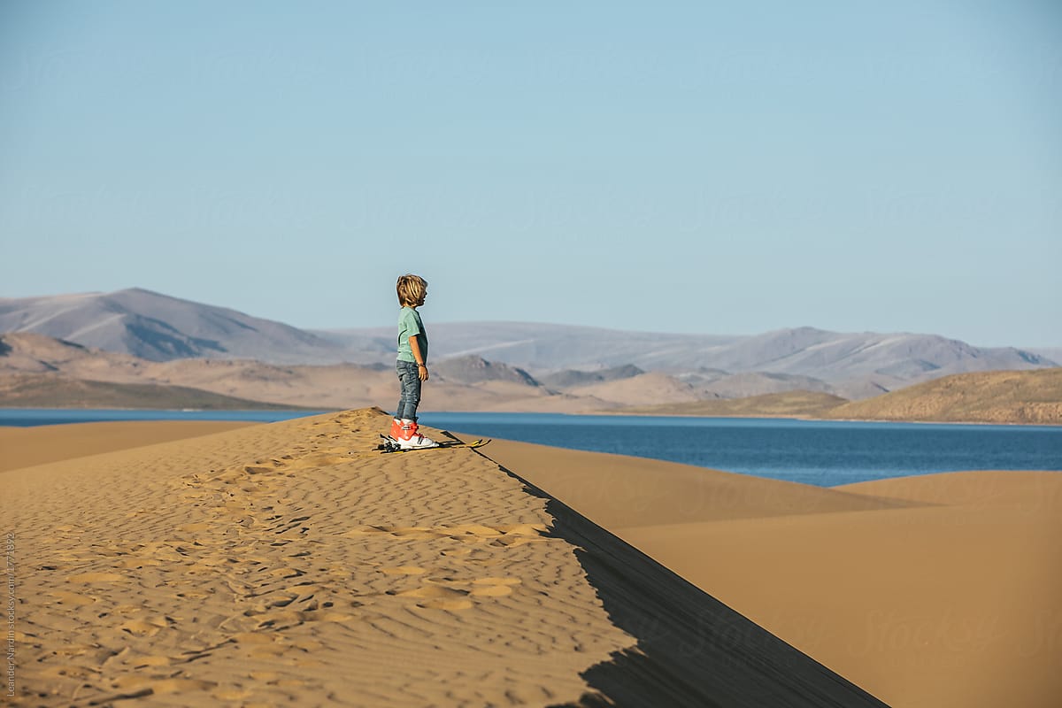 little boy with ski on top of a sand dune