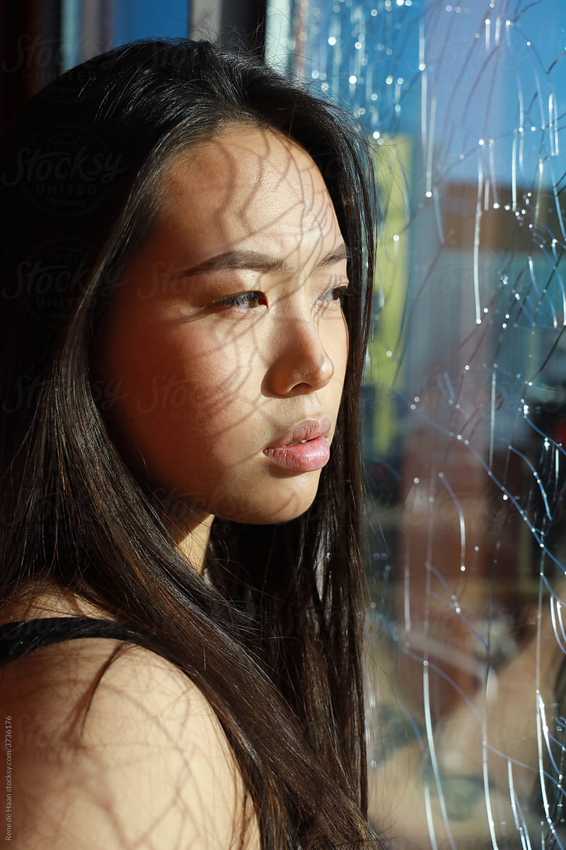 young Asian woman behind broken glass window