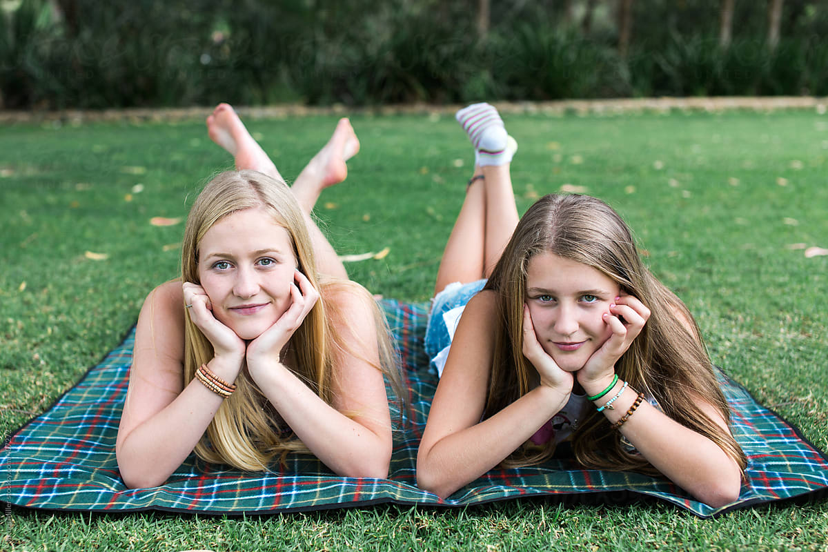 Two teen sisters lying on a picnic rug, looking directly at camera.