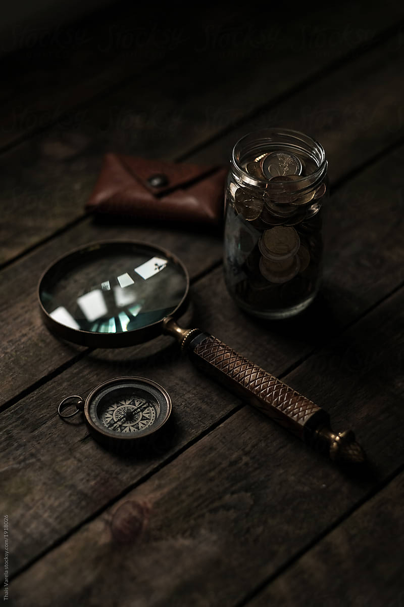 magnifying glass, compass, money jar and leather coin purse still life