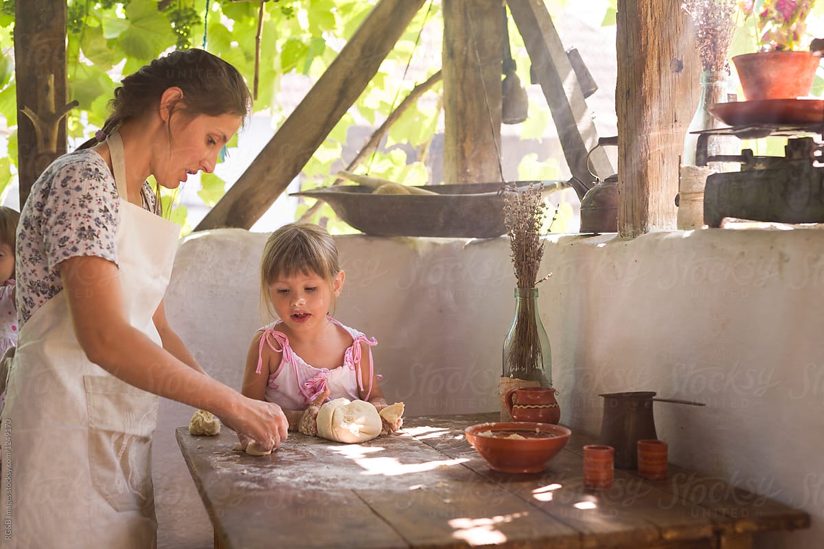 Mother and daughter kneading bread dough outdoor on the porch
