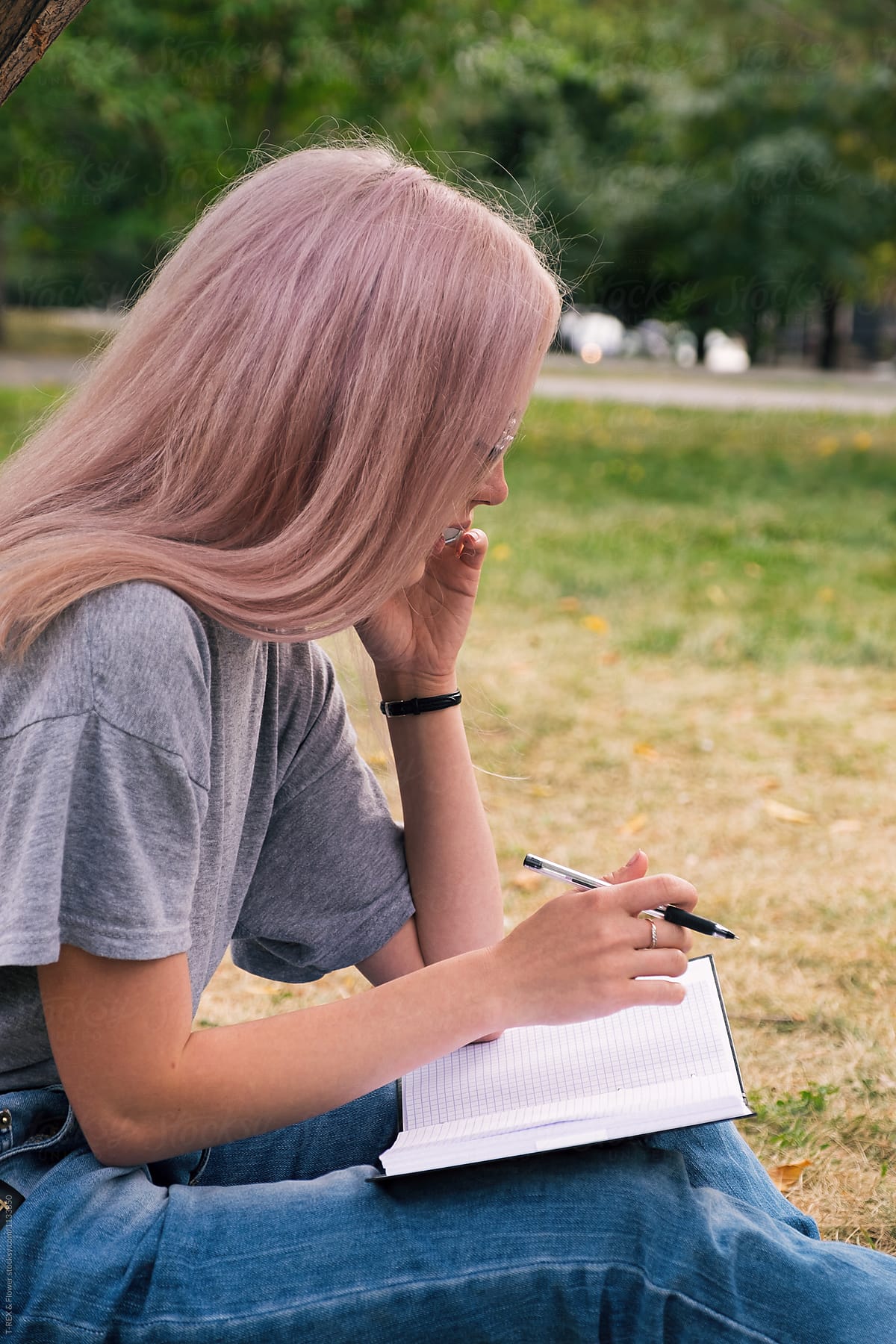 Pink-haired woman talking over phone and writing notes in notebook