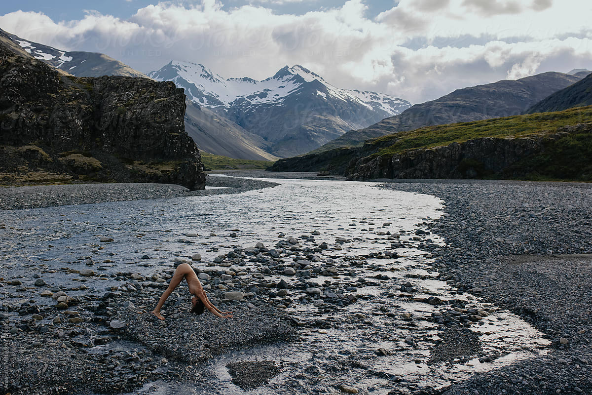 Naked slim woman doing yoga on the river in front of mountains