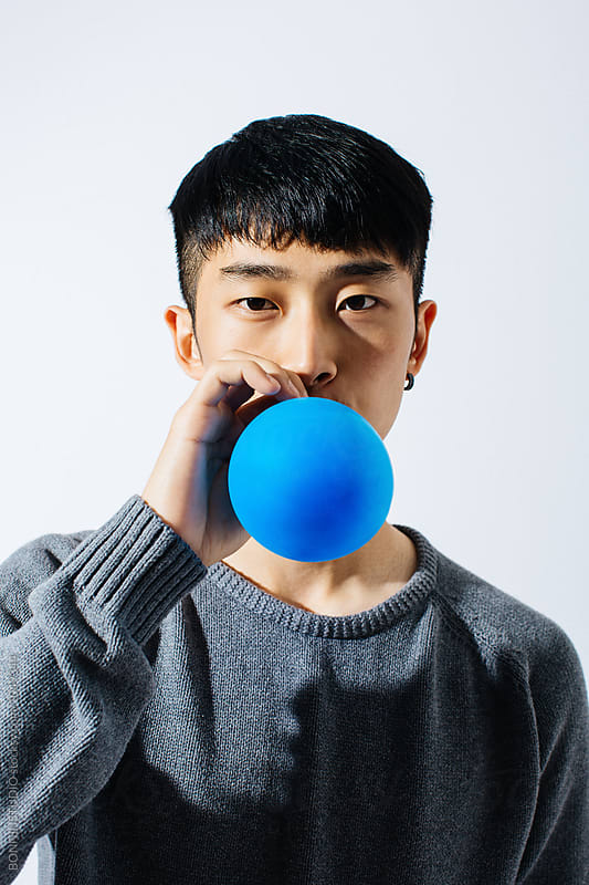 Asian man blowing a blue balloon over white background.