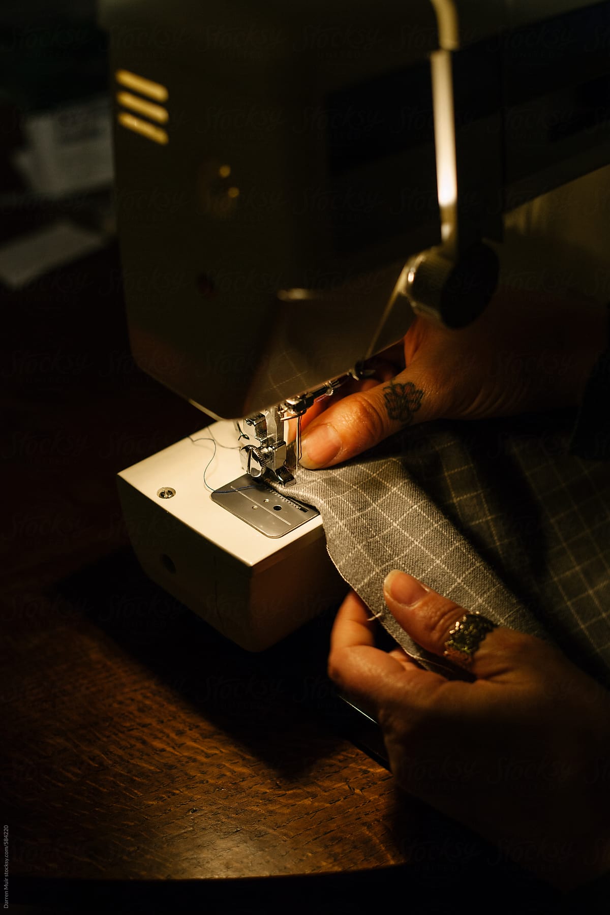 Woman\'s hand working on her electric sewing machine at night.