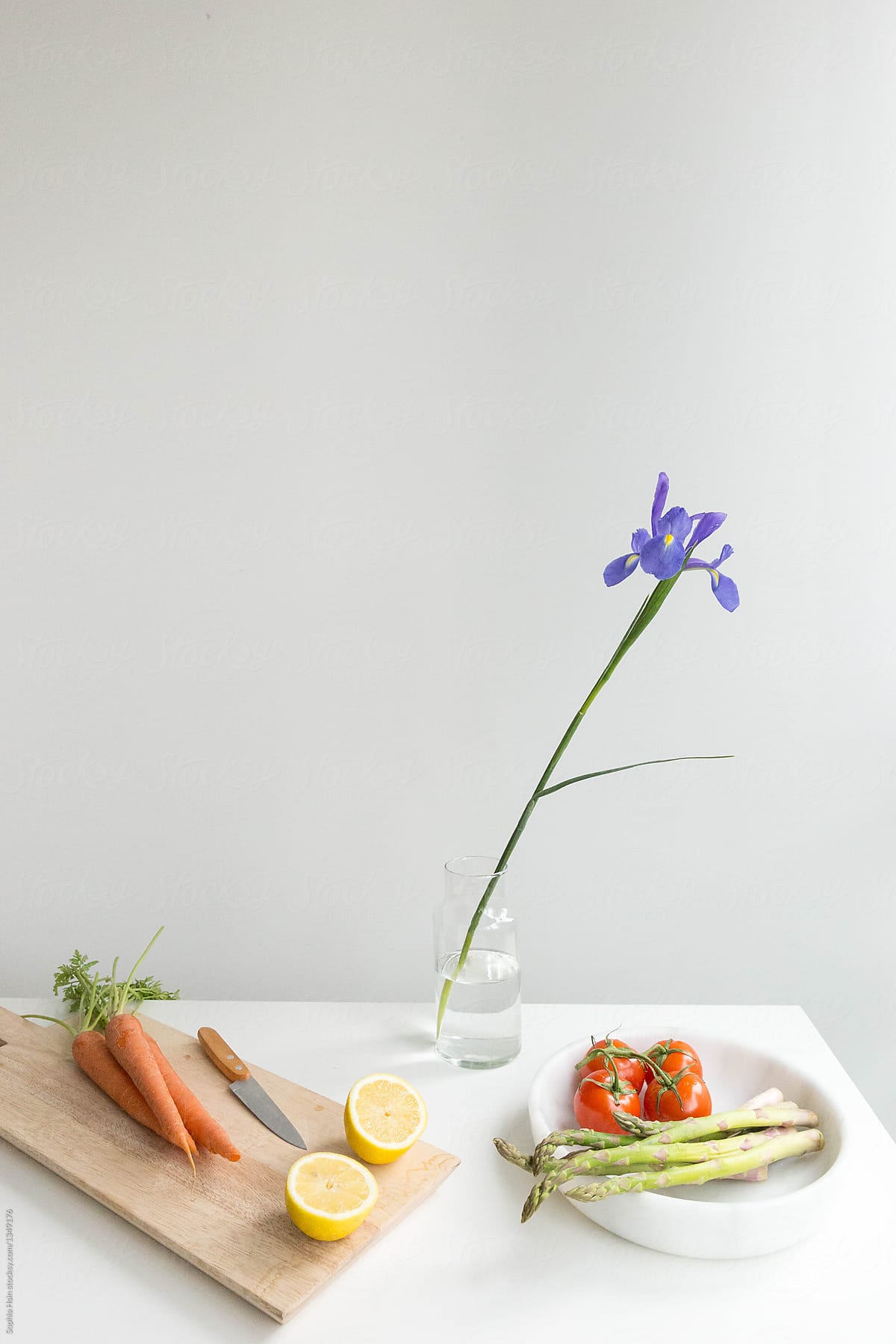 Vegetables on white table with single stem of purple iris
