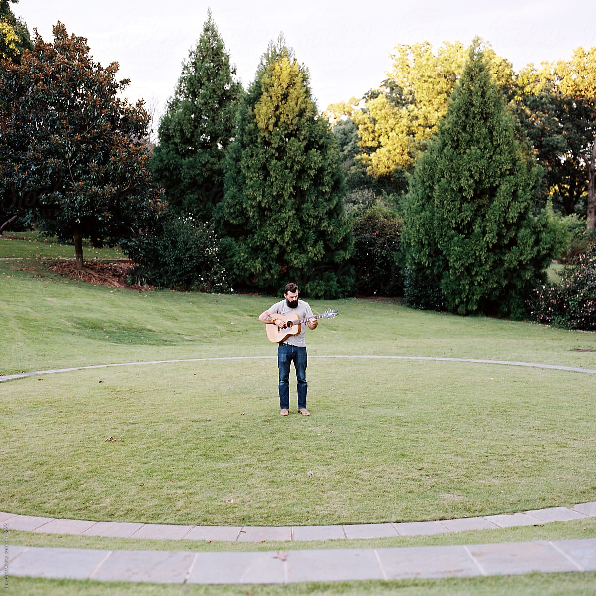 Bearded man with a guitar standing in a park