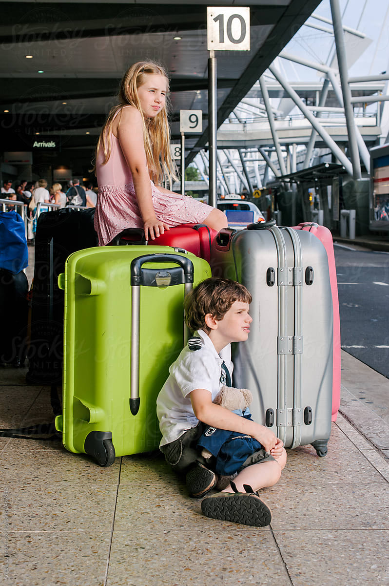 Two children and suitcases kerbside at a busy airport arrivals pick up point