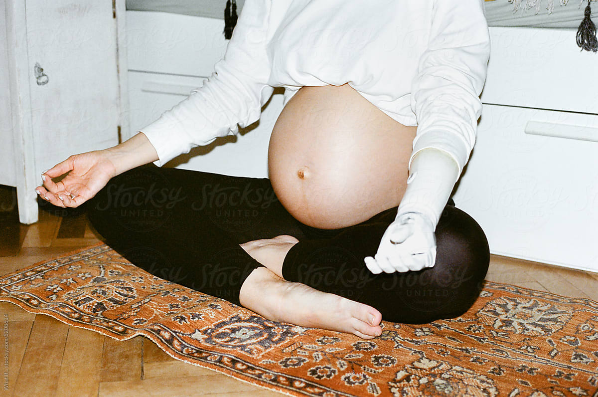 Close up pregnant woman sitting in Lotus position on carpet.