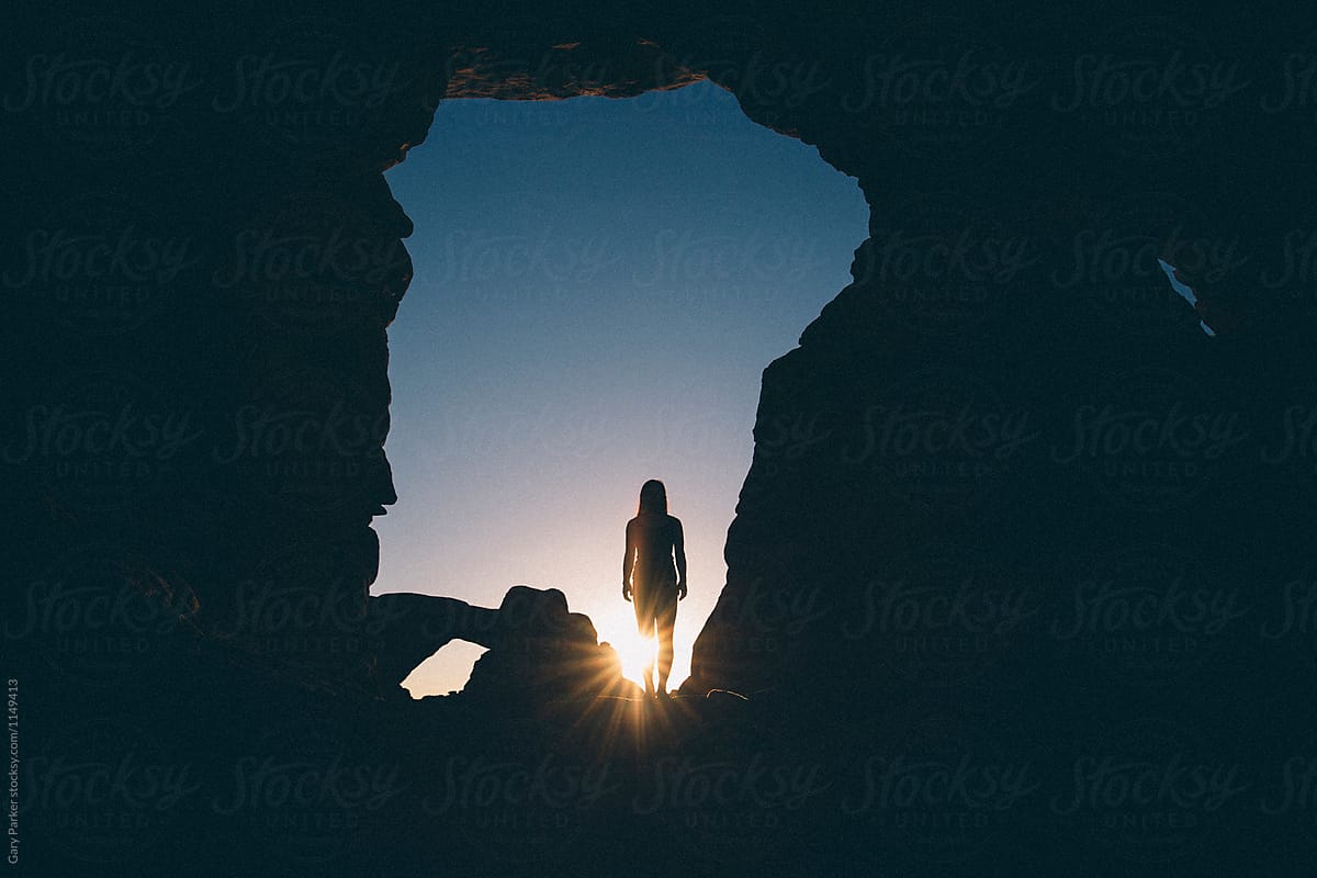 A woman stretching beneath a rock arch cave on sunrise
