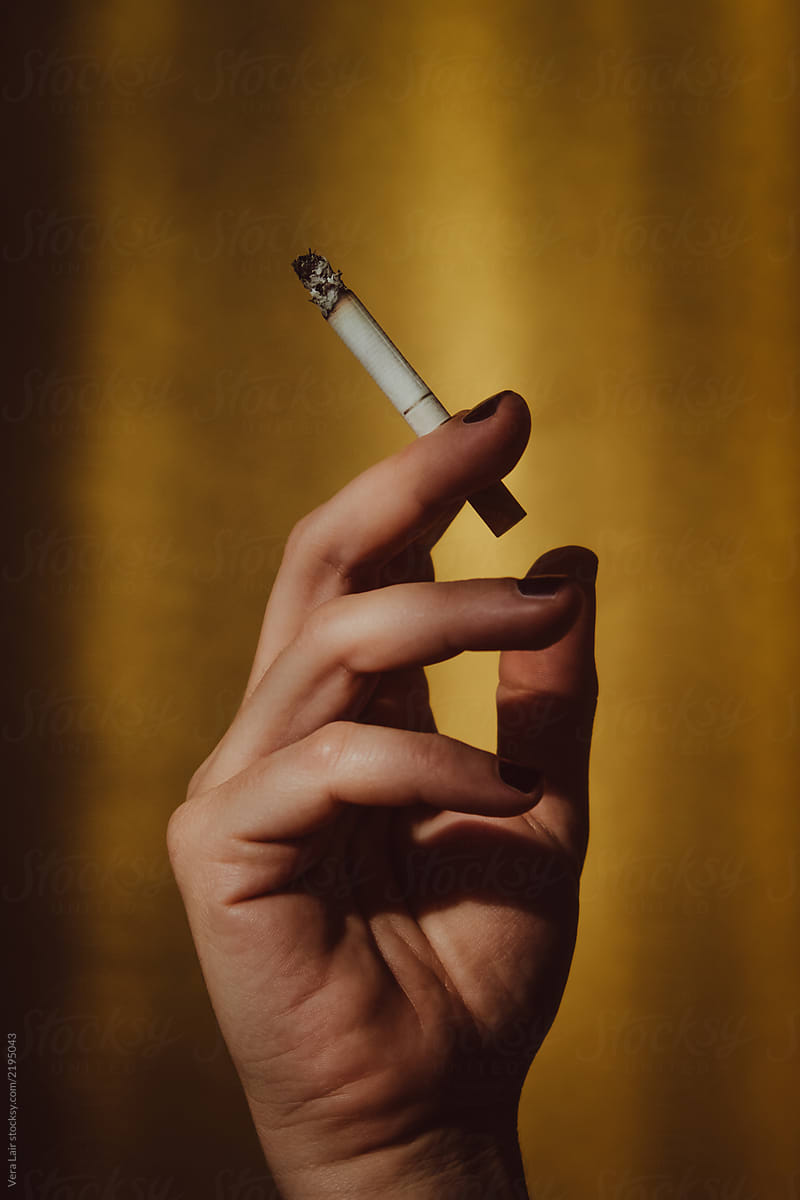 woman's hand holding a cigarette on a golden background