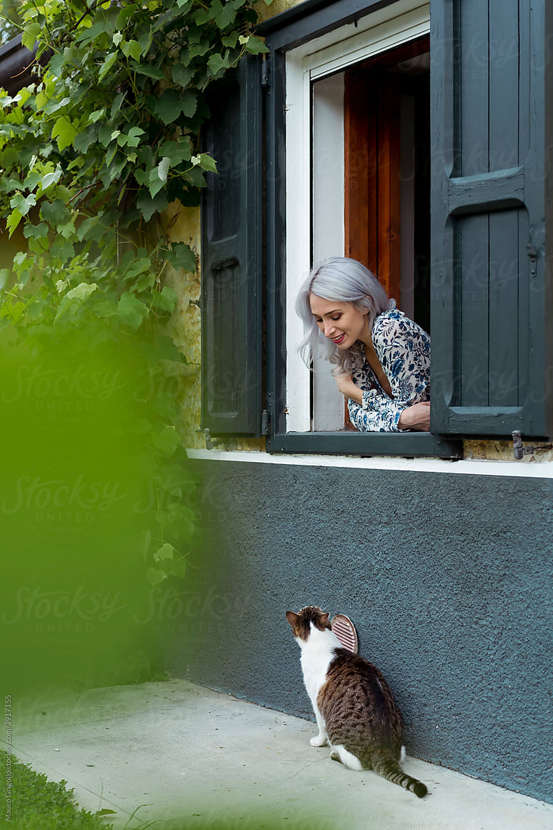 A woman at the window is looking at her cat outdoor