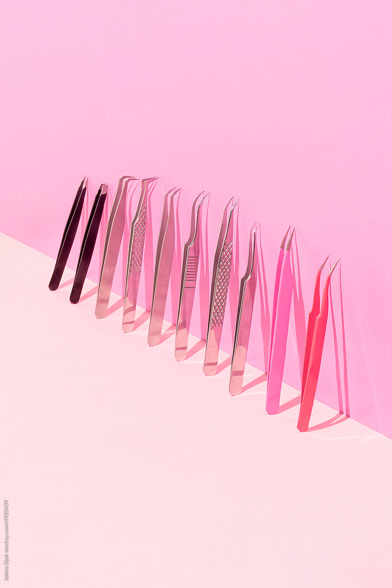 Various tweezers for fake eye lashes and brows leaning against pink.