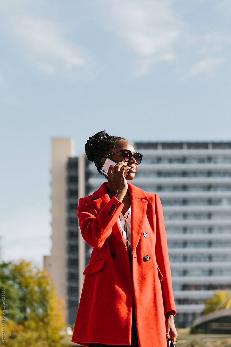 Stylish black businesswoman in red jacket speaking on smartphone
