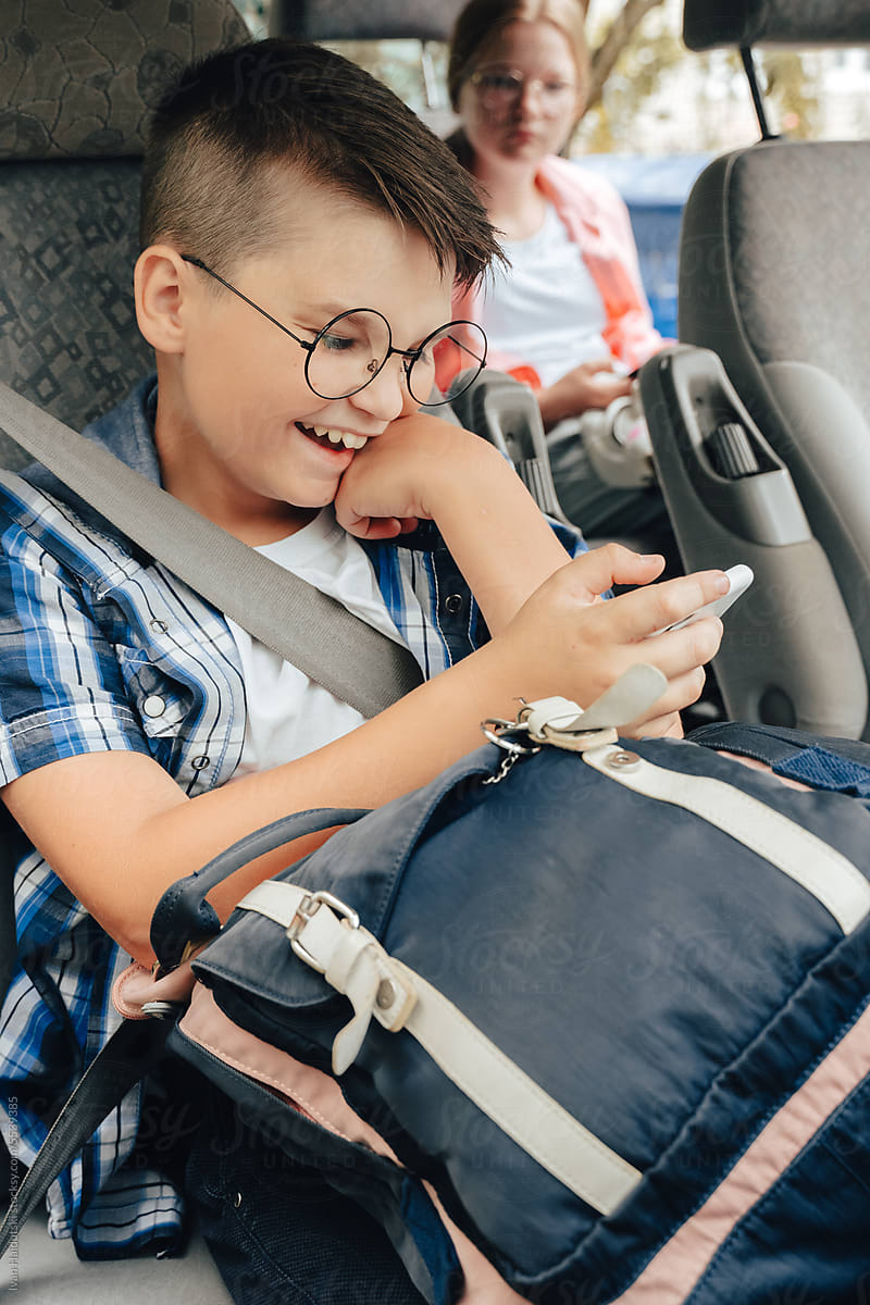 Laughing boy with backpack holding phone in car on way to school