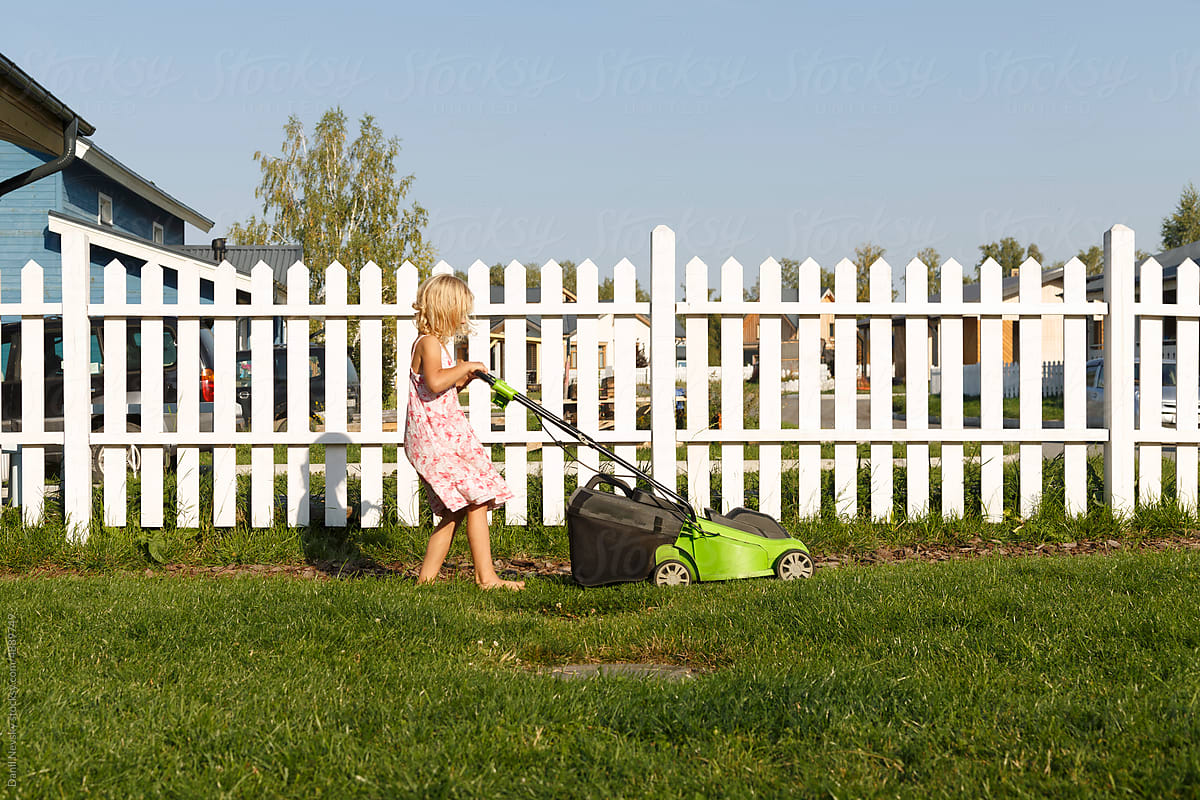 Child cutting grass with mower near fence