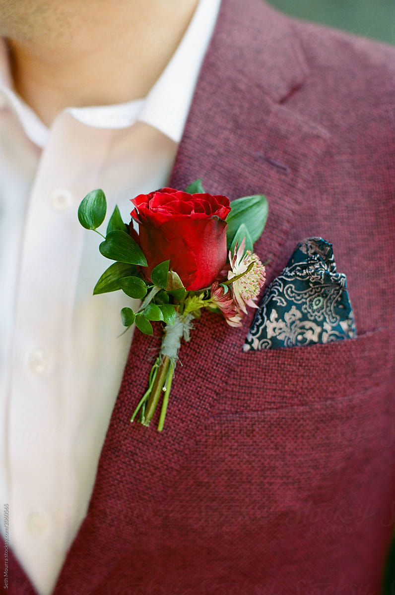 A red rose boutonniere up close against a maroon jacket