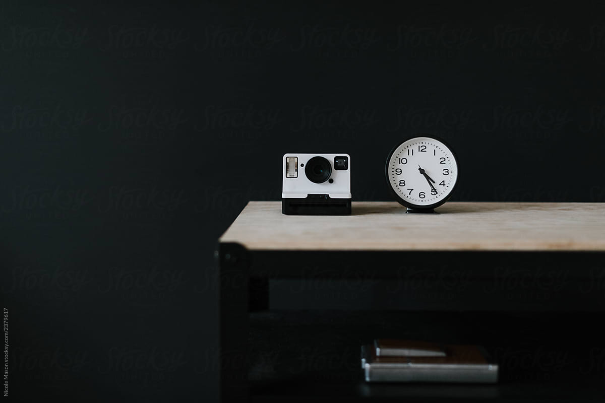 instant polaroid camera and analog clock on desk in front of black wall