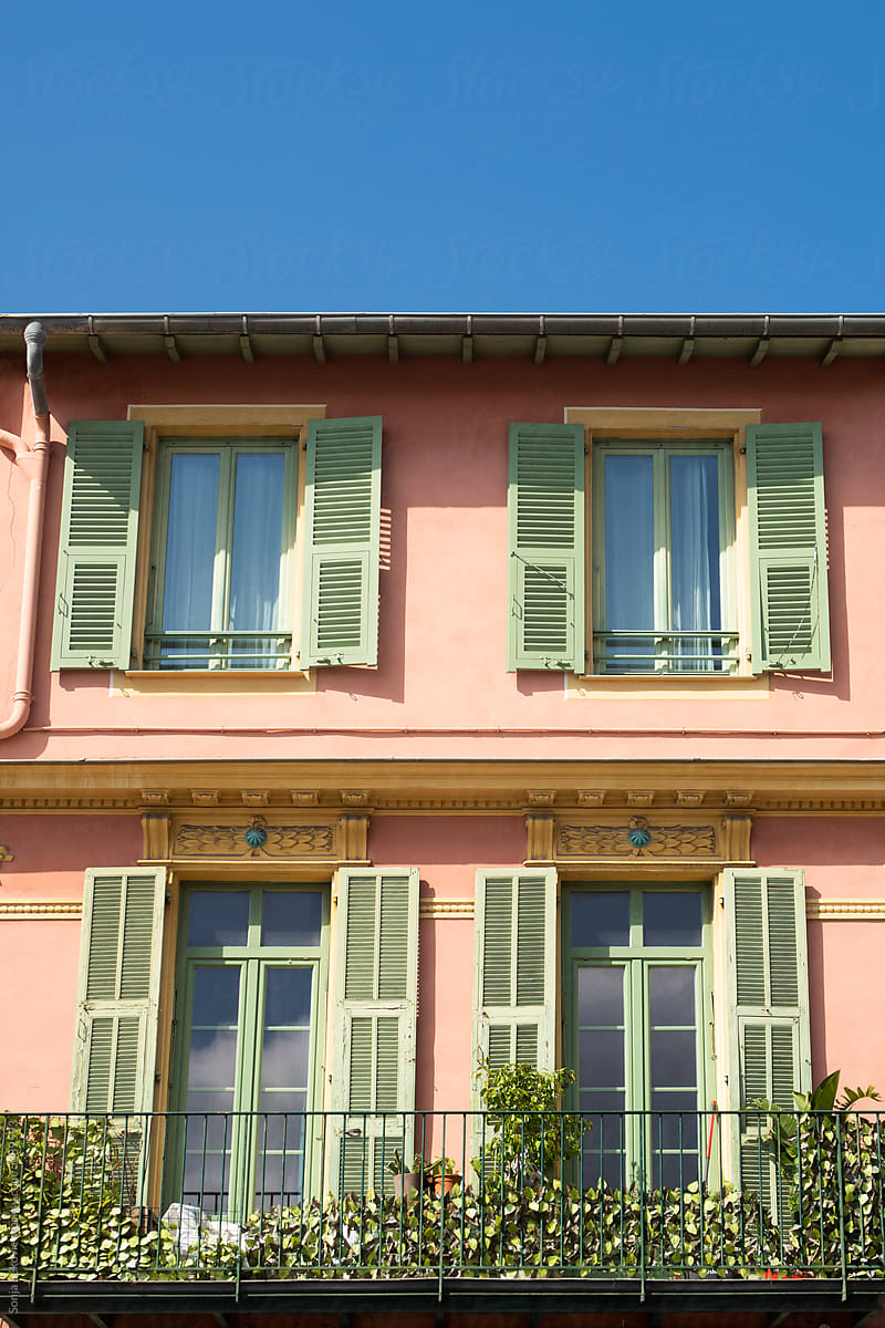 stylish pink building facade with green window shades and blue sky