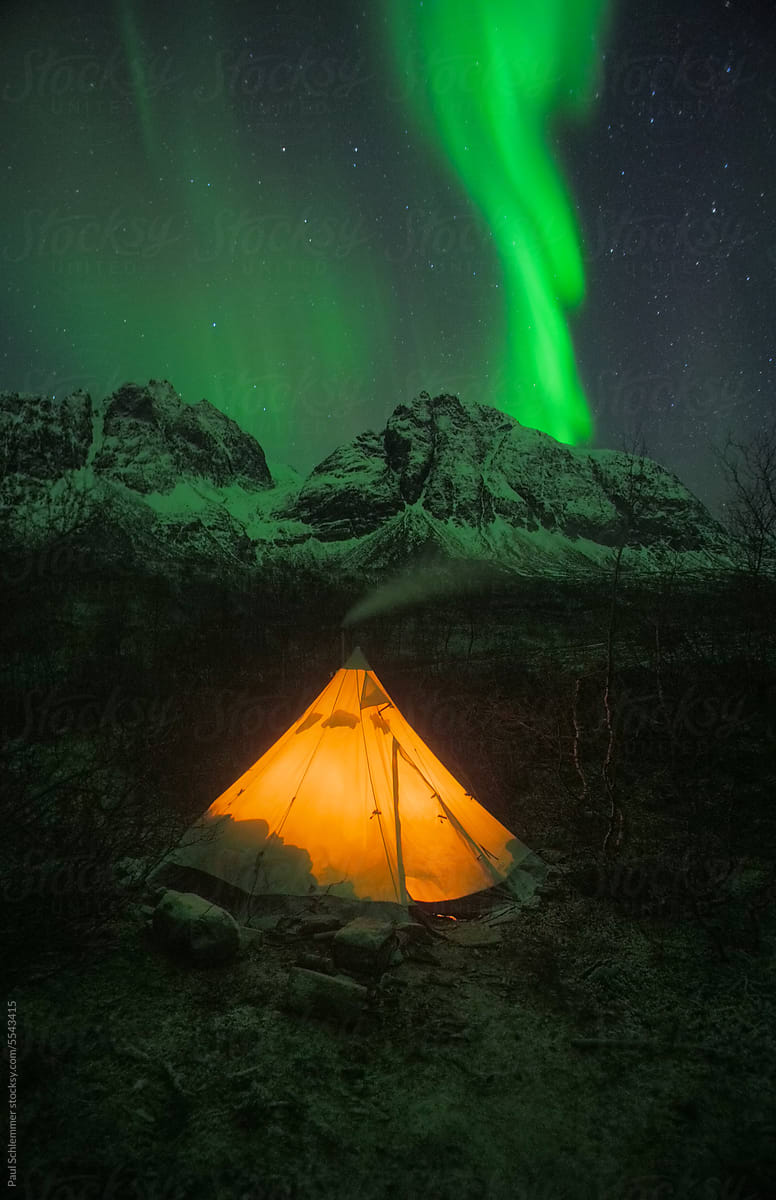Winter camping, glowing canvas tent under aurora northern lights